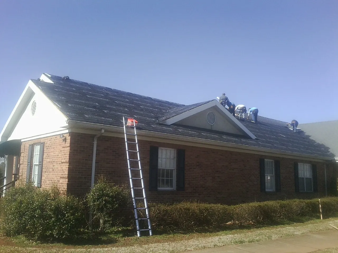 Crew tearing shingles off a brick ranch roof with a ladder set — Metal Roof Repair work by our crew in Charlotte