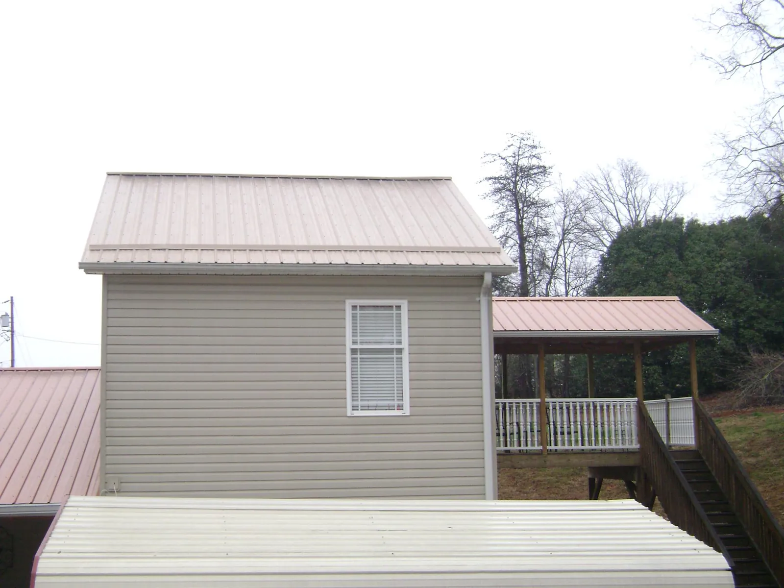 Tan metal roofs on a two story addition and attached porch, from a Roof Replacement job in Charlotte